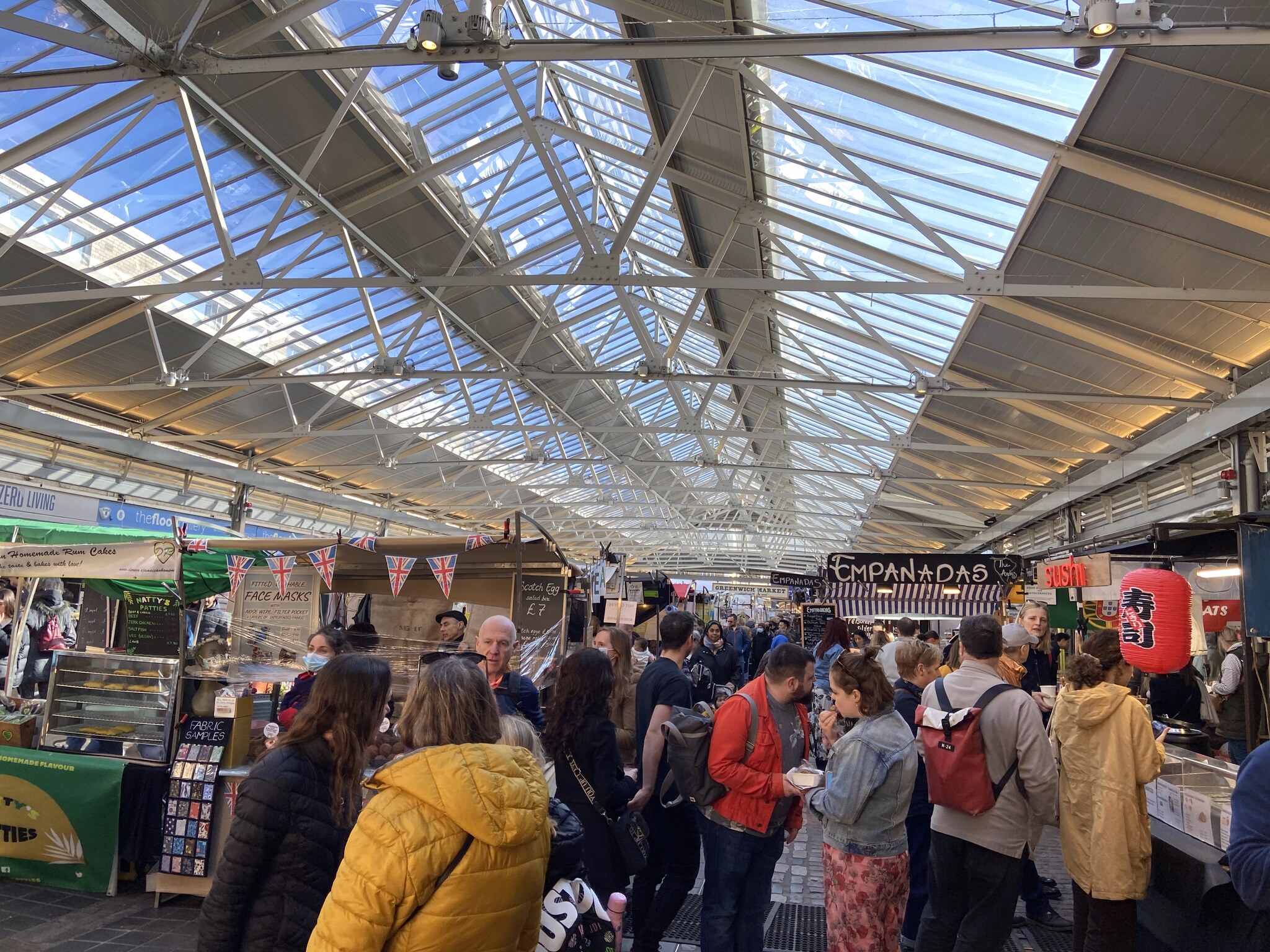 Het bruisende interieur van Greenwich Market met streetfood-kramen onder een glazen overkapping op een drukke weekenddag