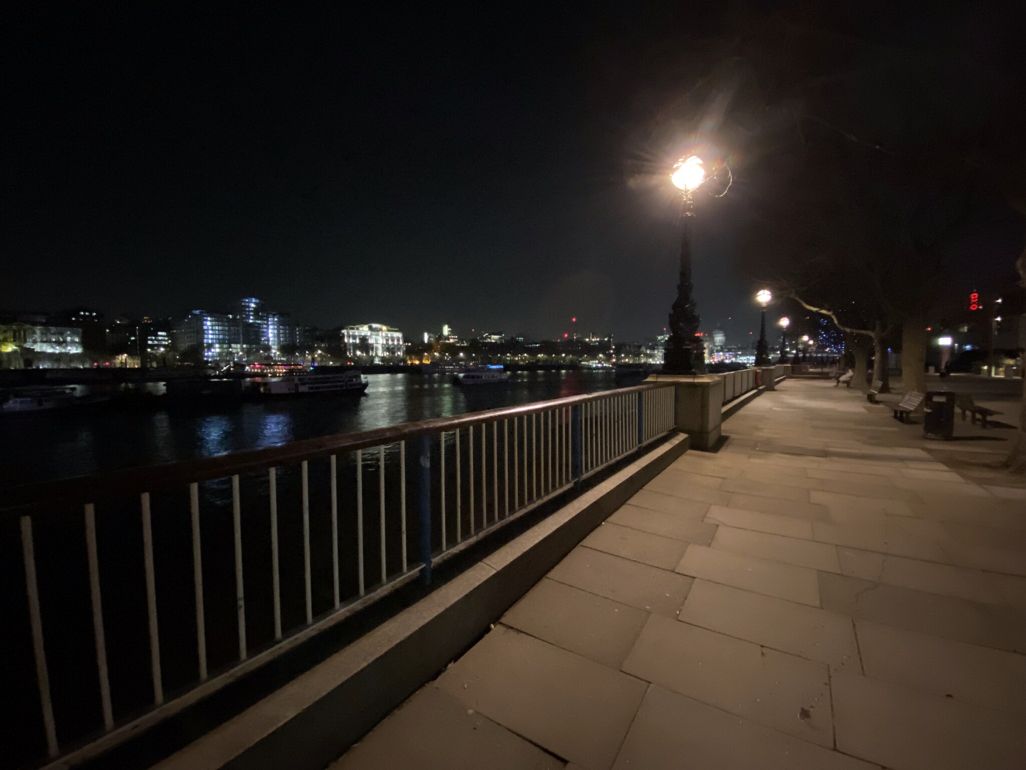 De Thames-promenade op South Bank bij nacht met een klassieke lantaarnpaal en de weerspiegeling van de stadslichten in het water