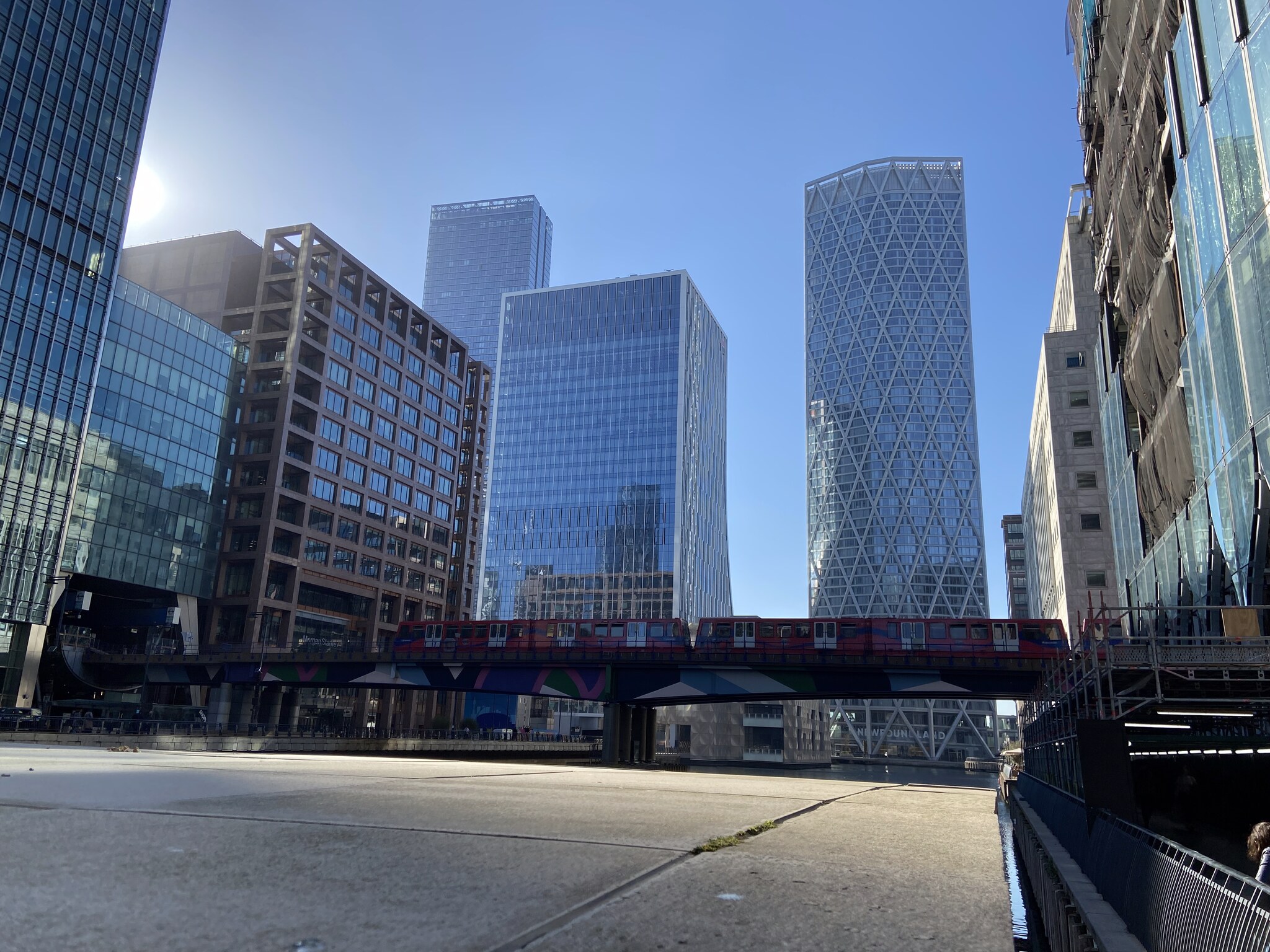 De Canary Wharf skyline gezien vanuit de voormalige dokken, met het DLR-viaduct op de voorgrond en glasgevels die reflecteren in het water