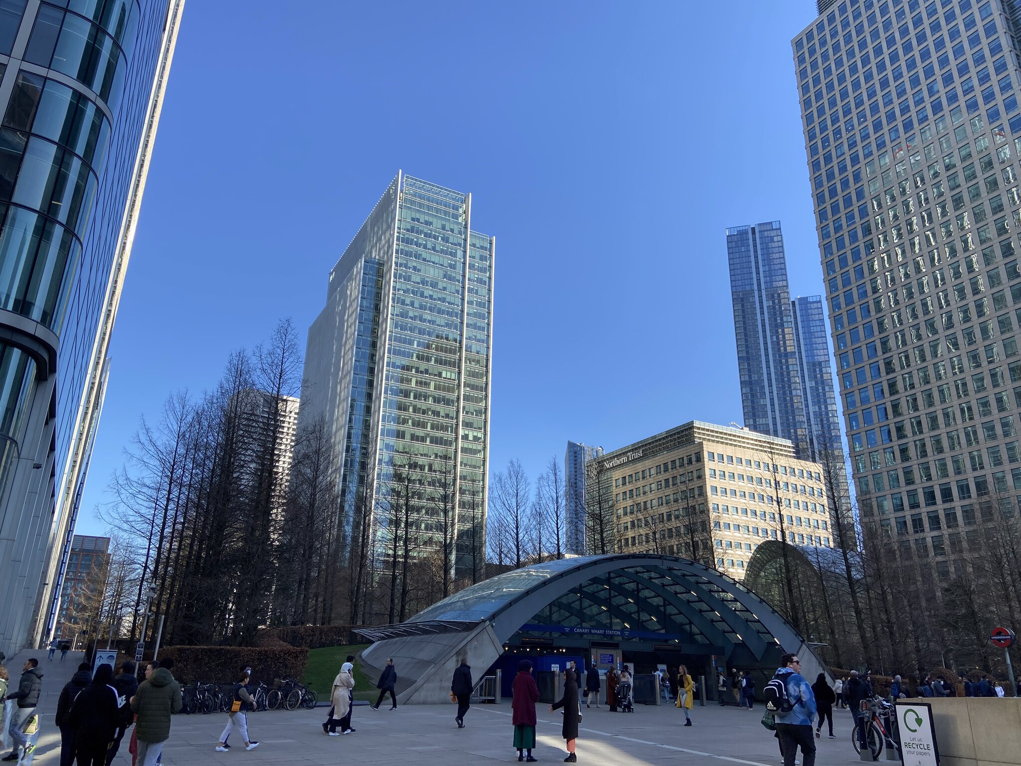 Breed overzicht van de Canary Wharf plaza met meerdere kantoortorens en de ondergrondse Jubilee Line-ingang van het station