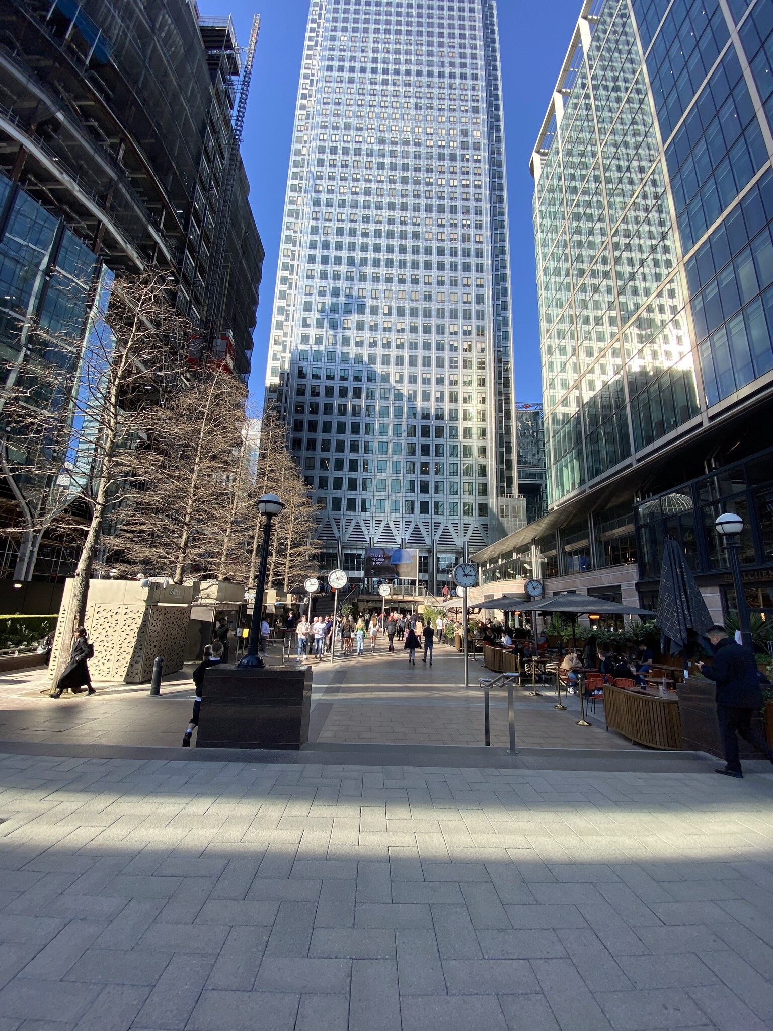 Omhoog kijkend naar de glazen wolkenkrabbers van Canary Wharf vanuit de plaza, met strakblauwe lucht ertussen